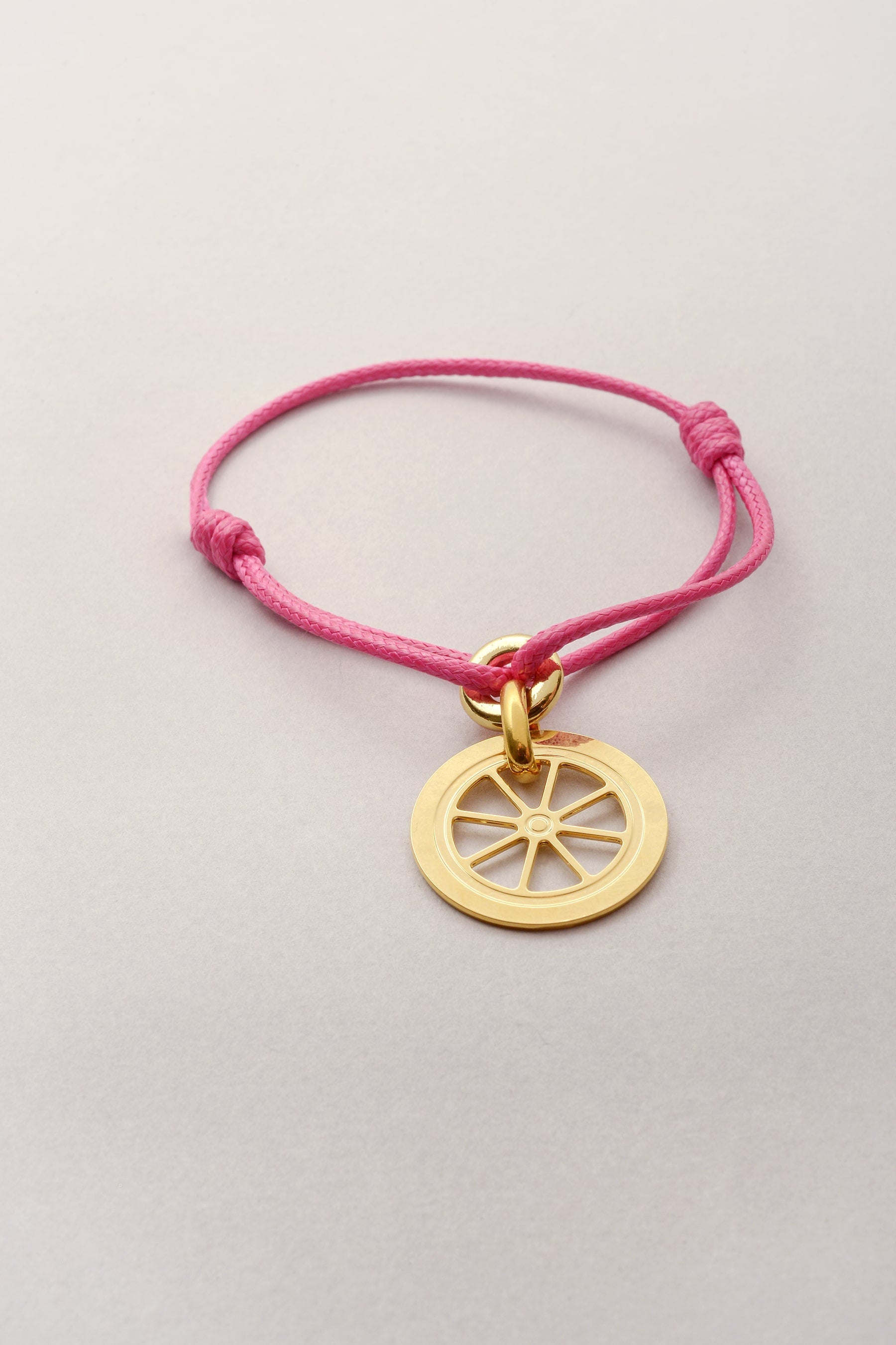 Ce bracelet se compose d'un cordon de coton coloré et d'un pendentif en forme de roue doré. Ajustable, ce bracelet fantaisie doré se règle grâce à deux noeuds coulissants. 