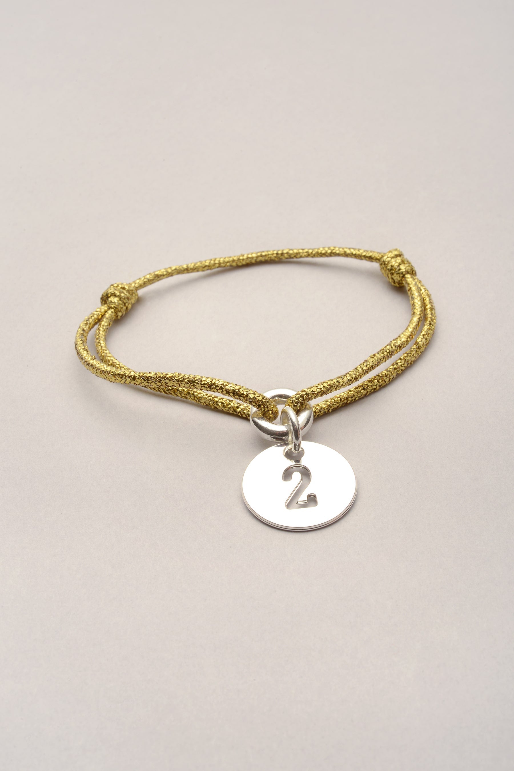 Ce bracelet se compose d'un cordon de coton coloré et d'une médaille avec un chiffre évidé. Bijou fantaisie argenté porte bonheur. Personnalisable dans la couleur de votre choix. 