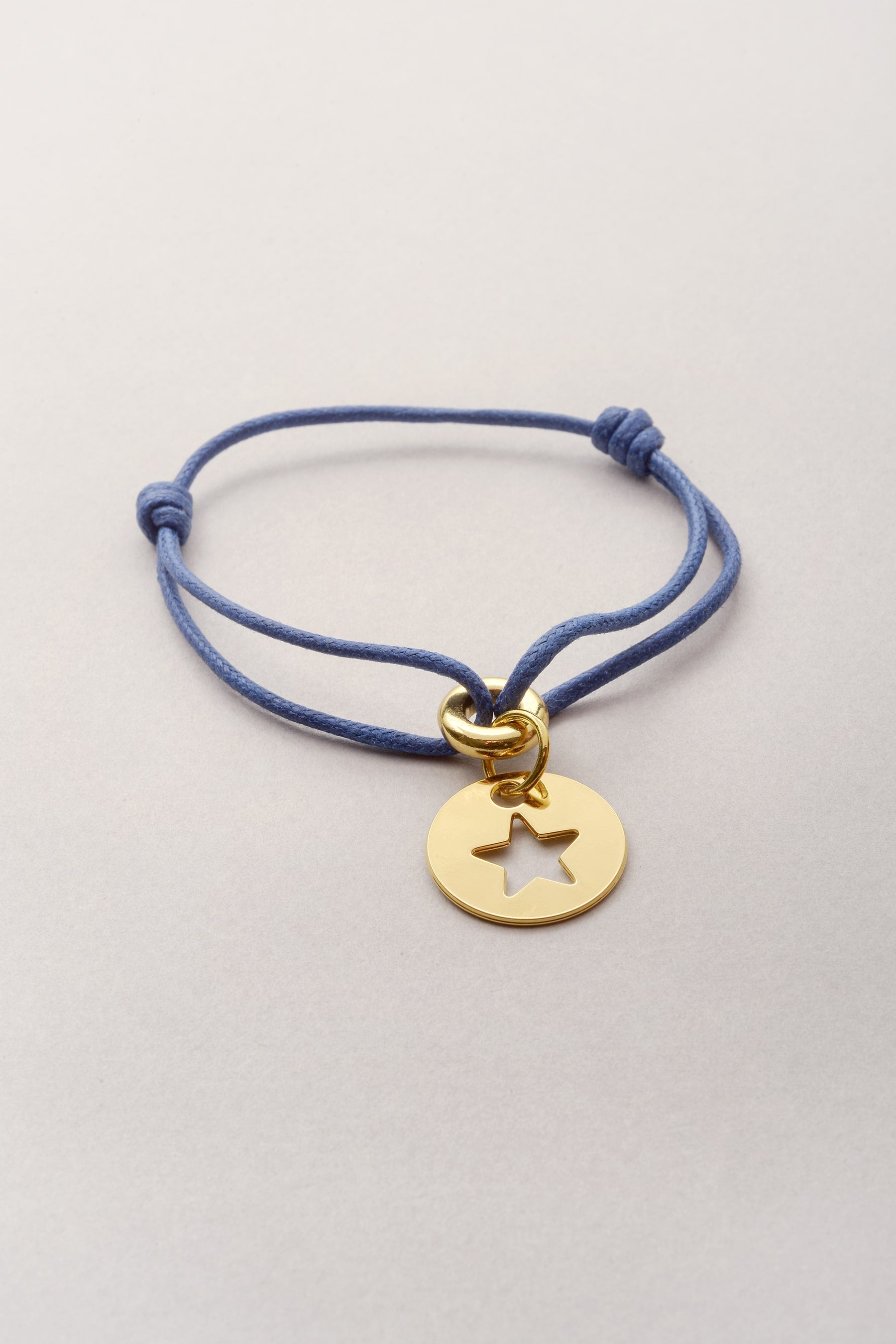 Ce bijou est composé d'un cordon de coton coloré et d'une médaille dorée avec une étoile évidée. Ajustable, ce bijou fantaisie doré se règle grâce à deux noeuds coulissants. 