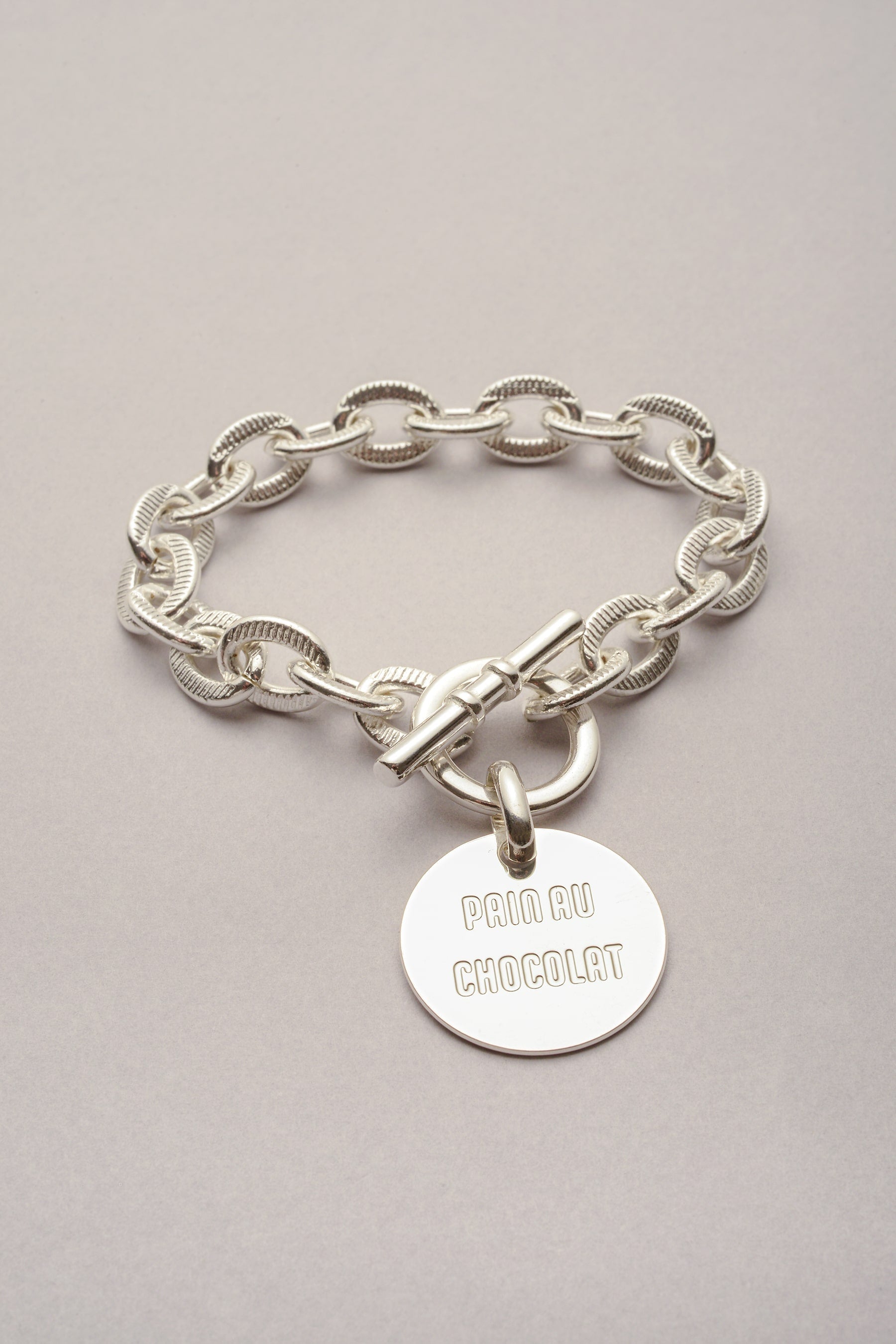 Le Bracelet Scarlett médaille Pain au Chocolat est une création artisanale. Bijou avec de la chaîne, un fermoir en T et une médaille gravée. 