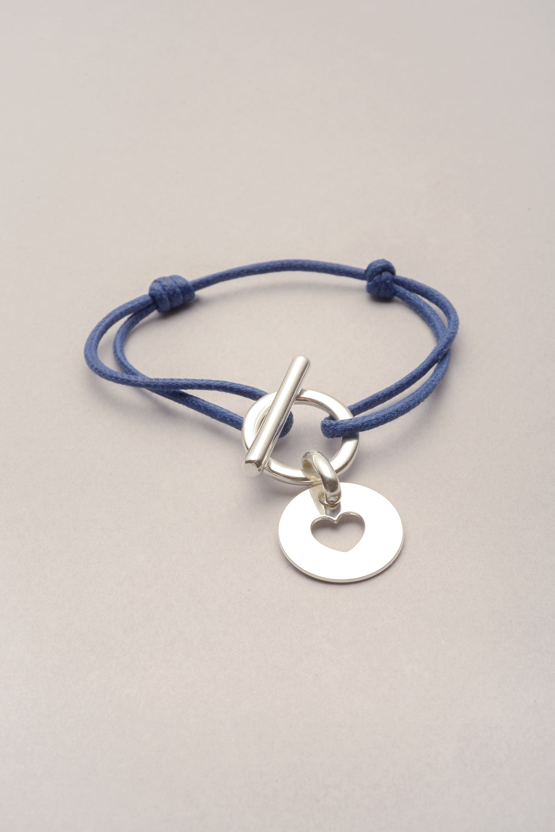 Ce bracelet est composé d'un bracelet cordon et d'une médaille avec un coeur évidé argenté. Pratique, le cordon est ajustable grâce à deux noeuds coulissants. 