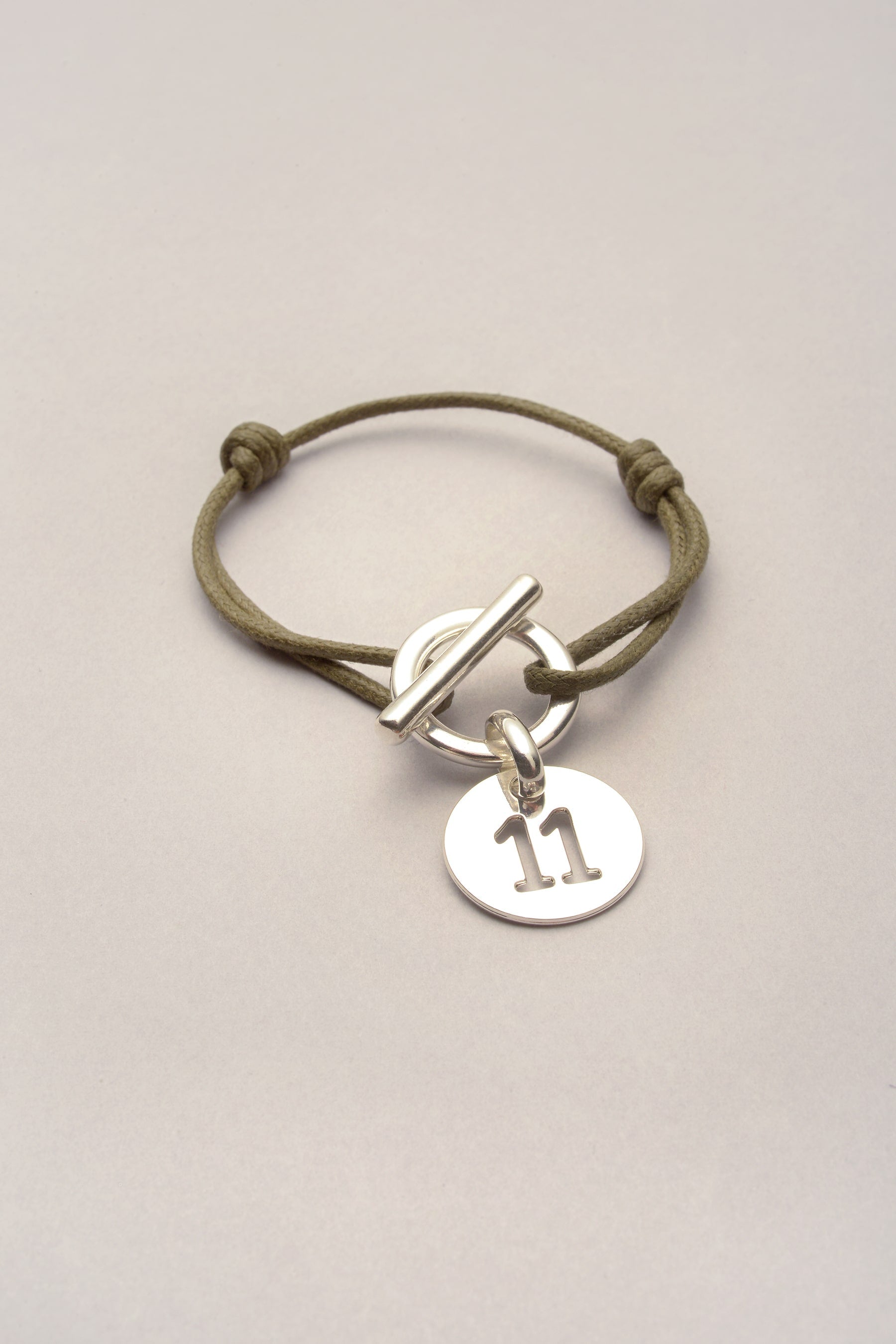 Ce bracelet attache médaille chiffre avec cordon de coton coloré est réglable. Pratique, il s'ajuste à l'aide de deux noeuds coulissants. La médaille chiffre est évidée, et existe de 1 à 12.