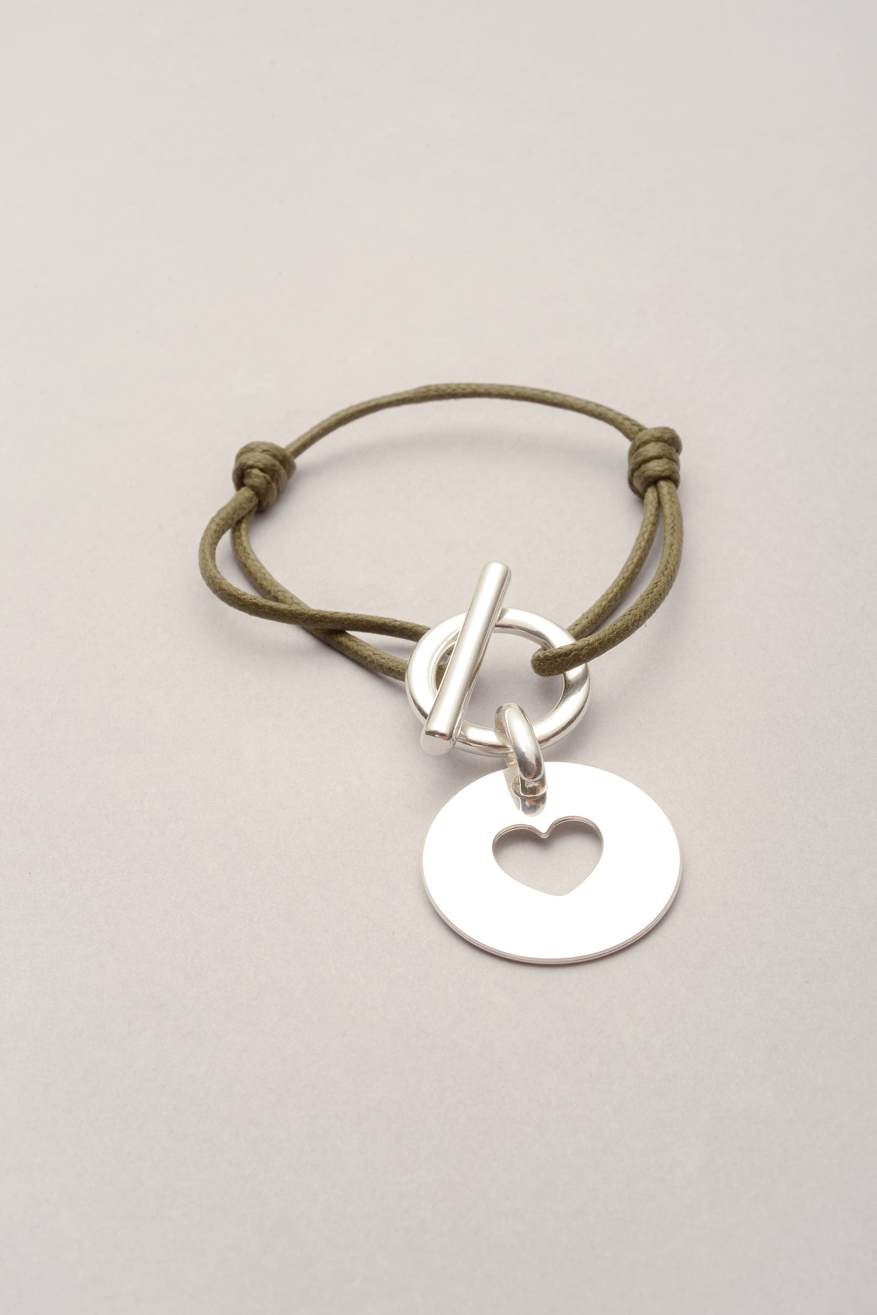 Ce bracelet est composé d'un cordon de coton coloré réglable et d'une médaille avec un coeur évidé. Ce bijou est pratique grâce à son système d'attache, il s'agit d'un fermoir en T. 