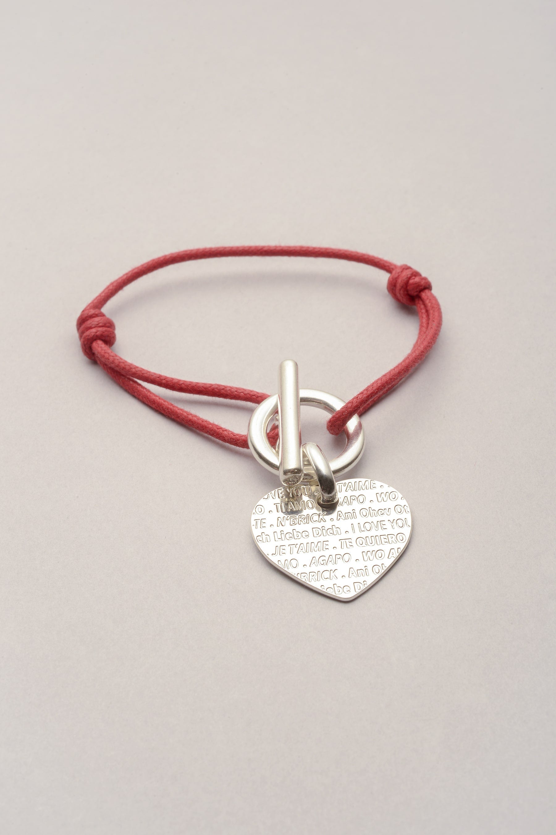 Bracelet argenté avec cordon de coton coloré et pendentif en forme de coeur. Sur le coeur on peut les la phrase je t'aime en plusieurs langues, inspiré du mur des je t'aime à Paris. Le bracelet s'ouvre et se ferme grâce à un fermoir en T. 