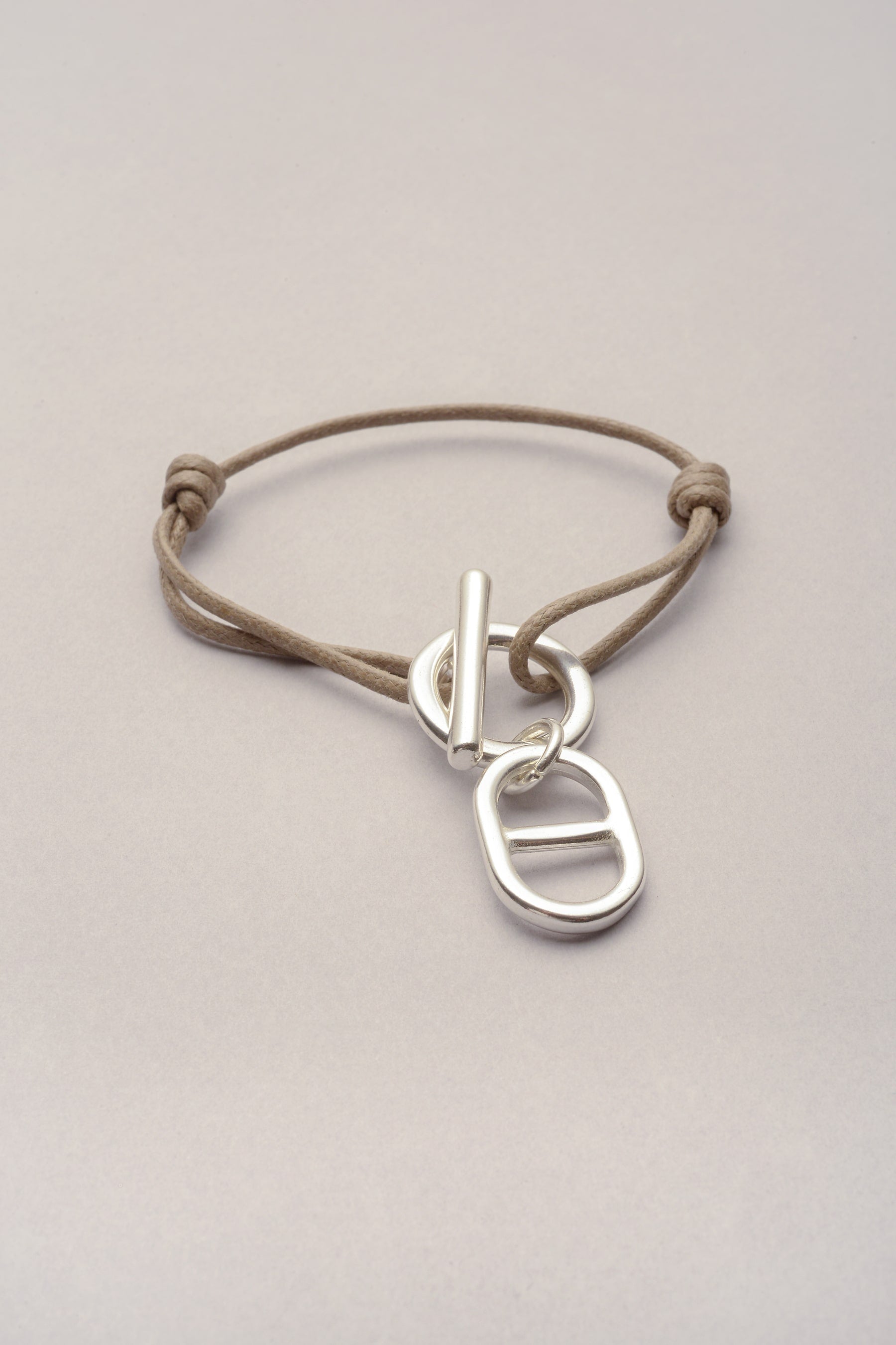 Ce bracelet est composé d'un cordon de coton coloré ajustable avec deux noeuds coulissants. Le bijou s'ouvre et se ferme avec une attache, qu'on appelle aussi "fermoir en T". Enfin, sur ce fermoir en T un pendentif est présent : la maille marine argenté. 