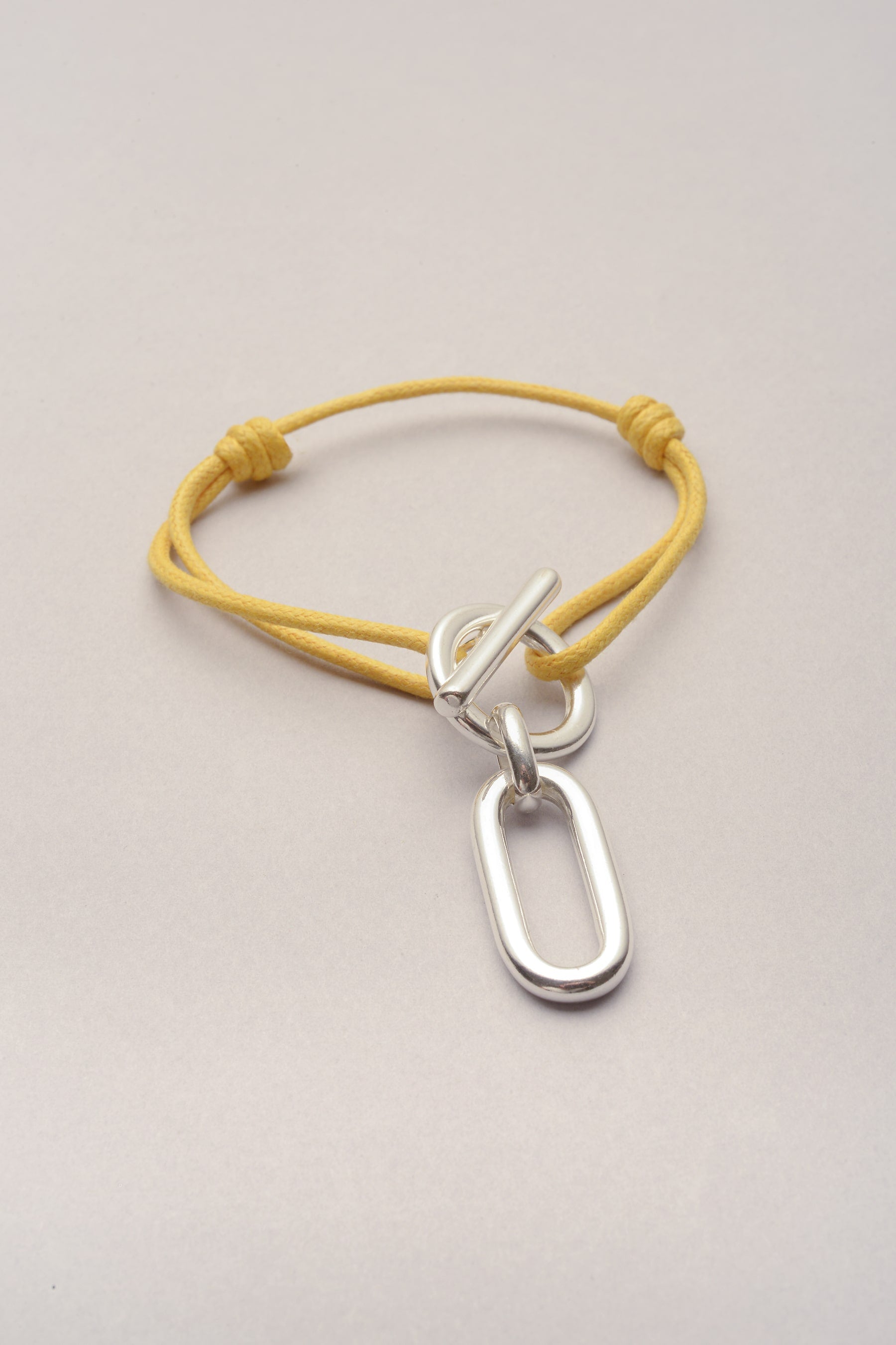 Ce bracelet est composé d'un cordon de coton coloré et d'une attache. L'atatche est un fermoir en T, ce qui rend pratique l'utilsiation du bijou. Sur le fermoir en T, un pendentif est accroché. Ce pendentif, qu'on appelle "Ricky" est un pendentif rectangulaire aux cotés arrondis, presque oval. 