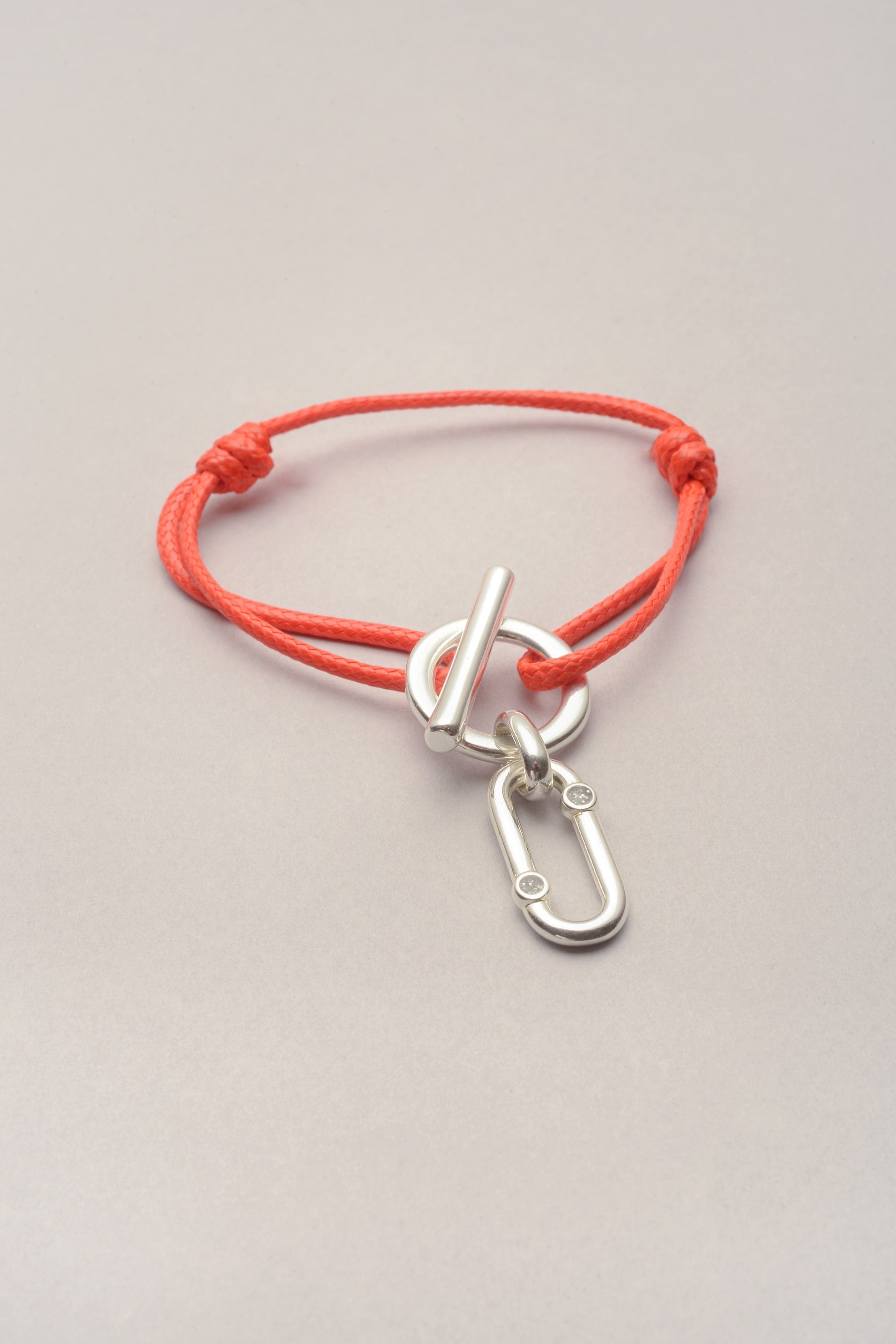 Ce bracelet est composé d'un cordon, d'un fermoir en T et d'un pendentif. le cordon est en coton coloré réglable grâce à deux noeuds coulissants. Sur l'attache un pendentif est présent: c'est le pendentif ricky strass. 