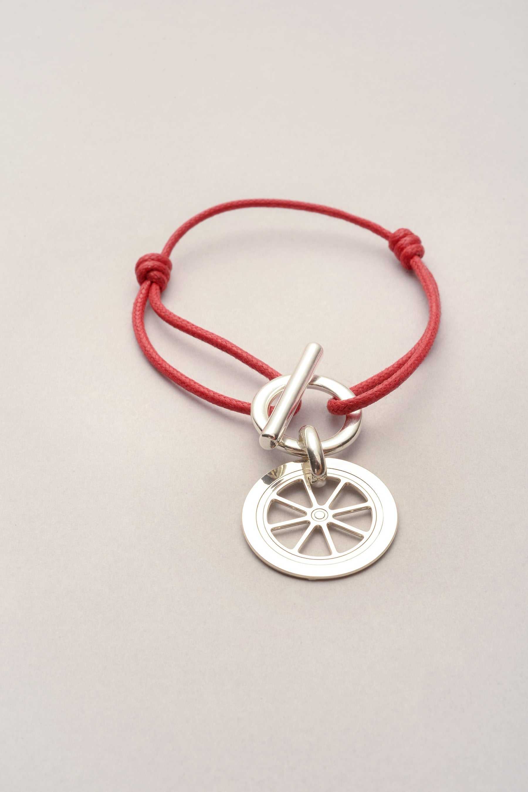 Ce bracelet est composé d'un cordon coloré et d'un pendentif roue. Réglable grâce a deux noeuds coulissants. 