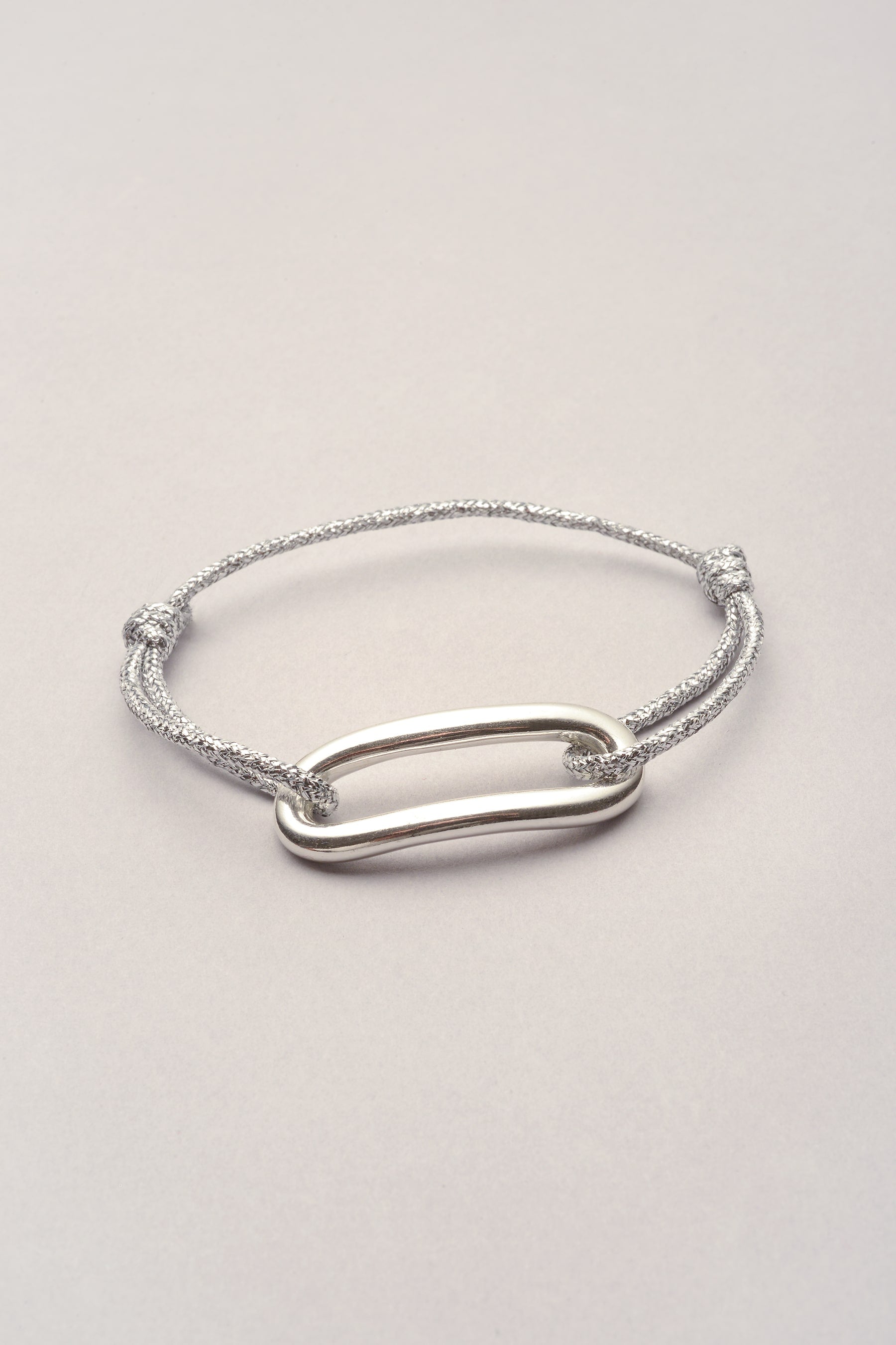 Ce bijou est composé d'un pendentif large en forme d'oval allongé recourbé et d'un cordon de coton. Réglable, ce bracelet s'ajuste au poignet grâce à ses deux noeuds coulissants. Mixte et personnalisable : c'est vous qui choisissez la couleur de cordon. 