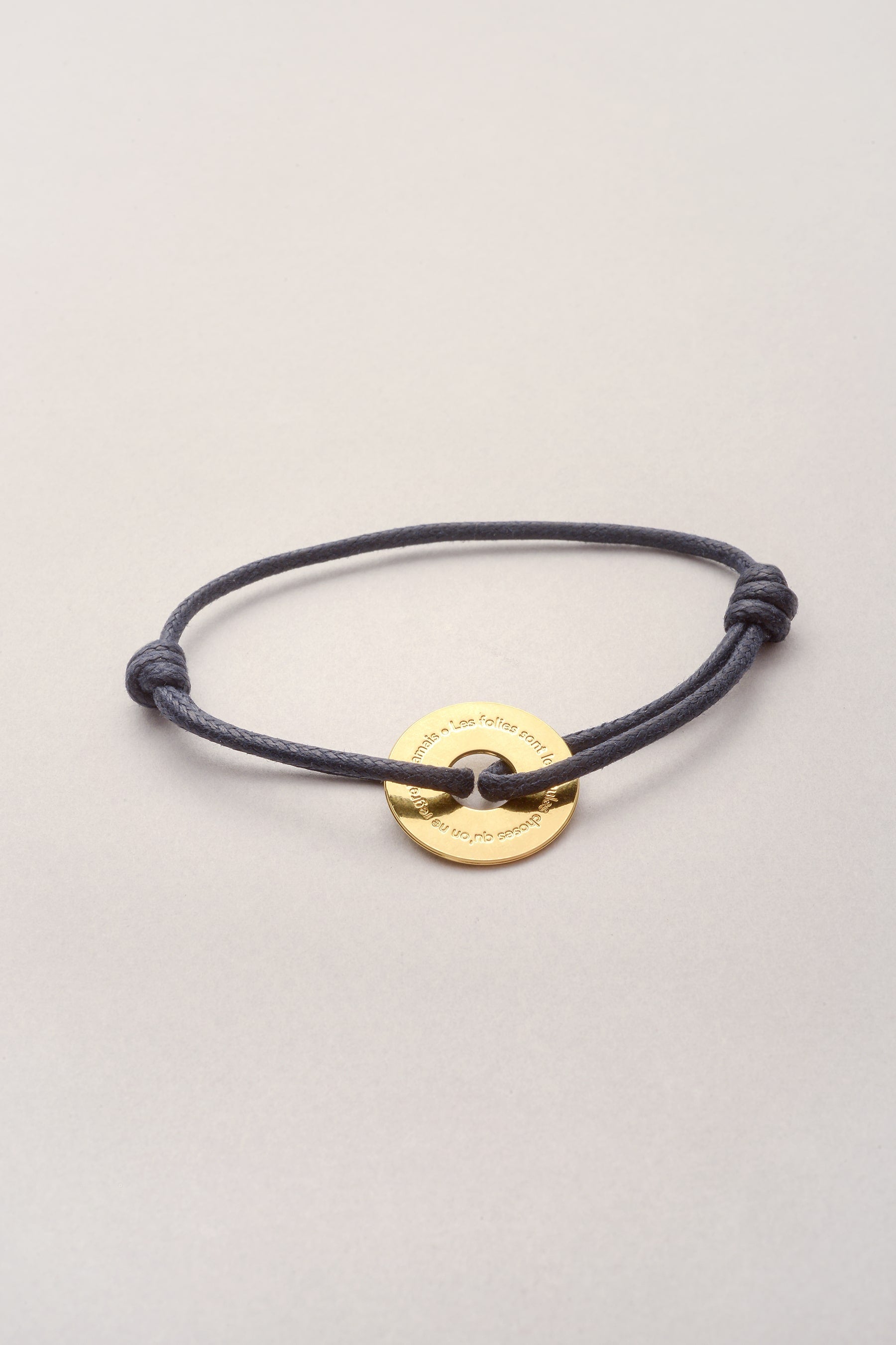 Ce bracelet est composé d'un pendentif en forme de disque sur lequel est inscrit une citation: les folies sont les seules choses qu'on ne regrette jamais. Ajustable, il est composé d'un cordon réglable. 