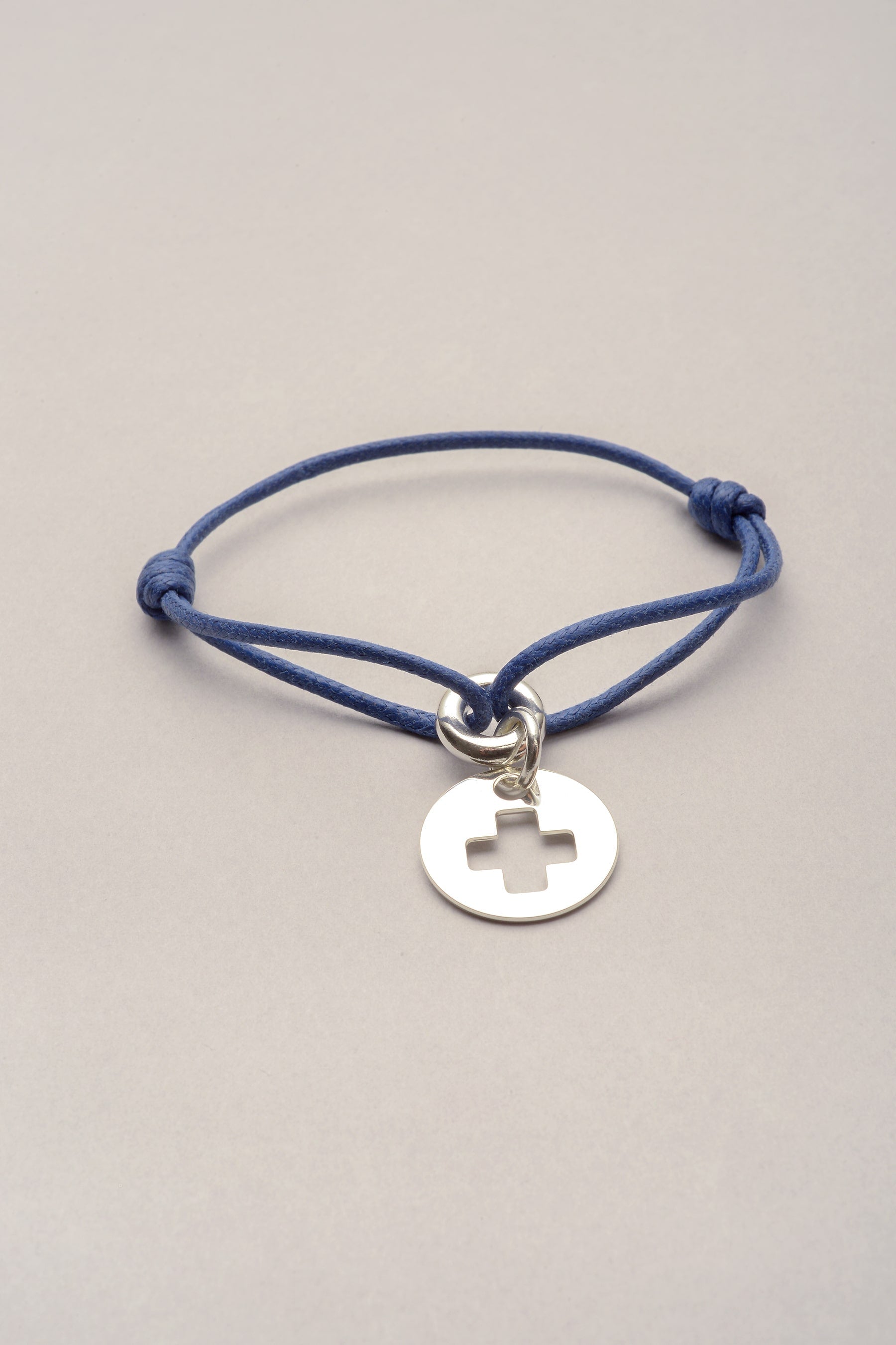 Ce bracelet est composé d'un cordond e coton coloré et d'une médaille ronde avec une croix évidée. Réglable, ce bijou fantaisie argenté est fabriqué en France. 