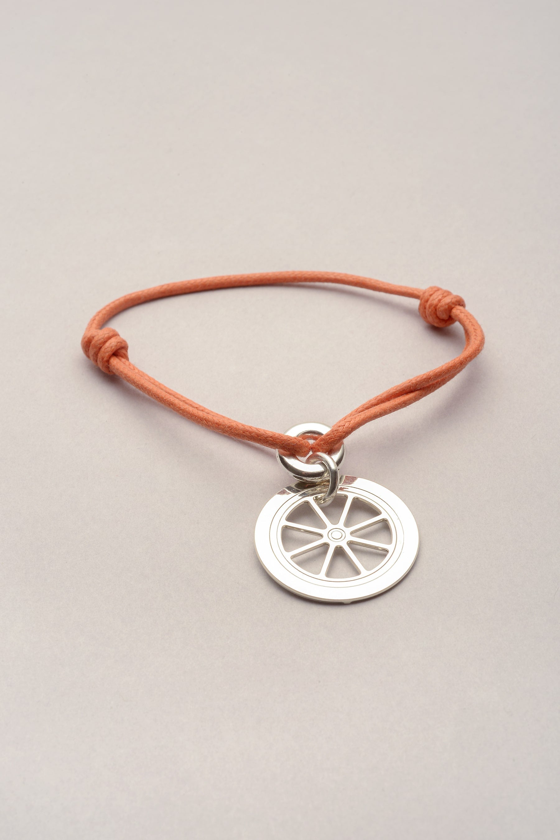 Ce bijou se compose d'un cordon de coton coloré et d'un pendentif roue argenté. La médaille roue s'inspire du triporteur Musardise. Réglable, ce bijou argenté fantaisie s'adapte à tous les poignets. 
