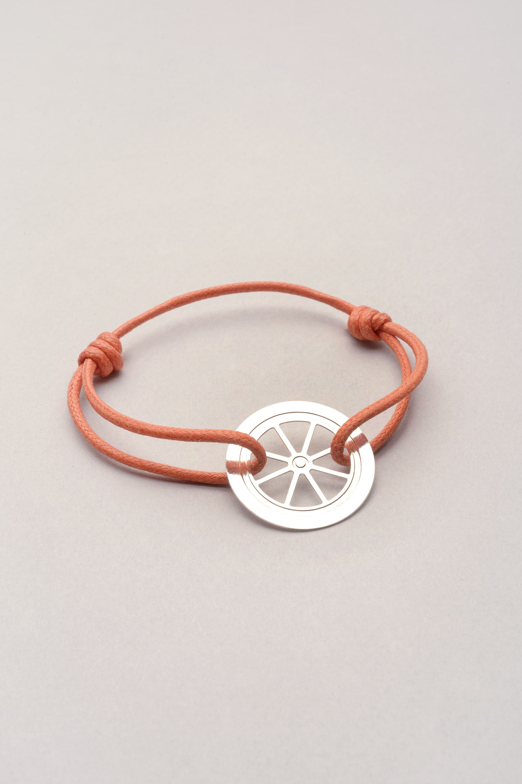 Ce bijou est composé d'un pendentif roue et d'un cordon de coton coloré. Sur la photo, le cordon est orange pêche, il existe aussi dans plusieurs coloris. En effet, ce bijou est personnalisable dans plein de couleurs. 