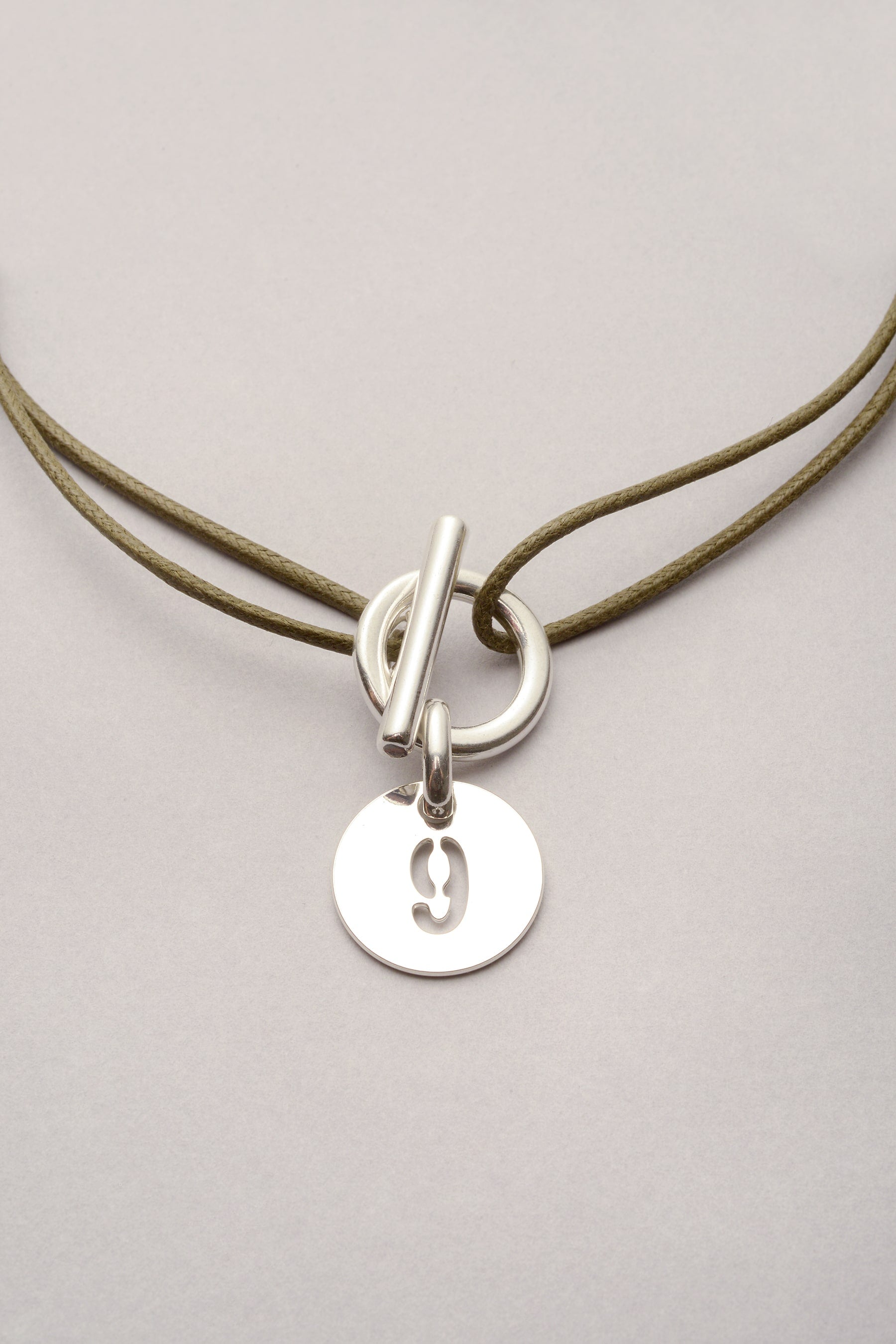 Ce collier est composé d'un cordon de coton coloré et d'une médaille avec un chiffre évidé. La médaille est positionnée sur l'attache, est mesure 20mm de diamètre. 