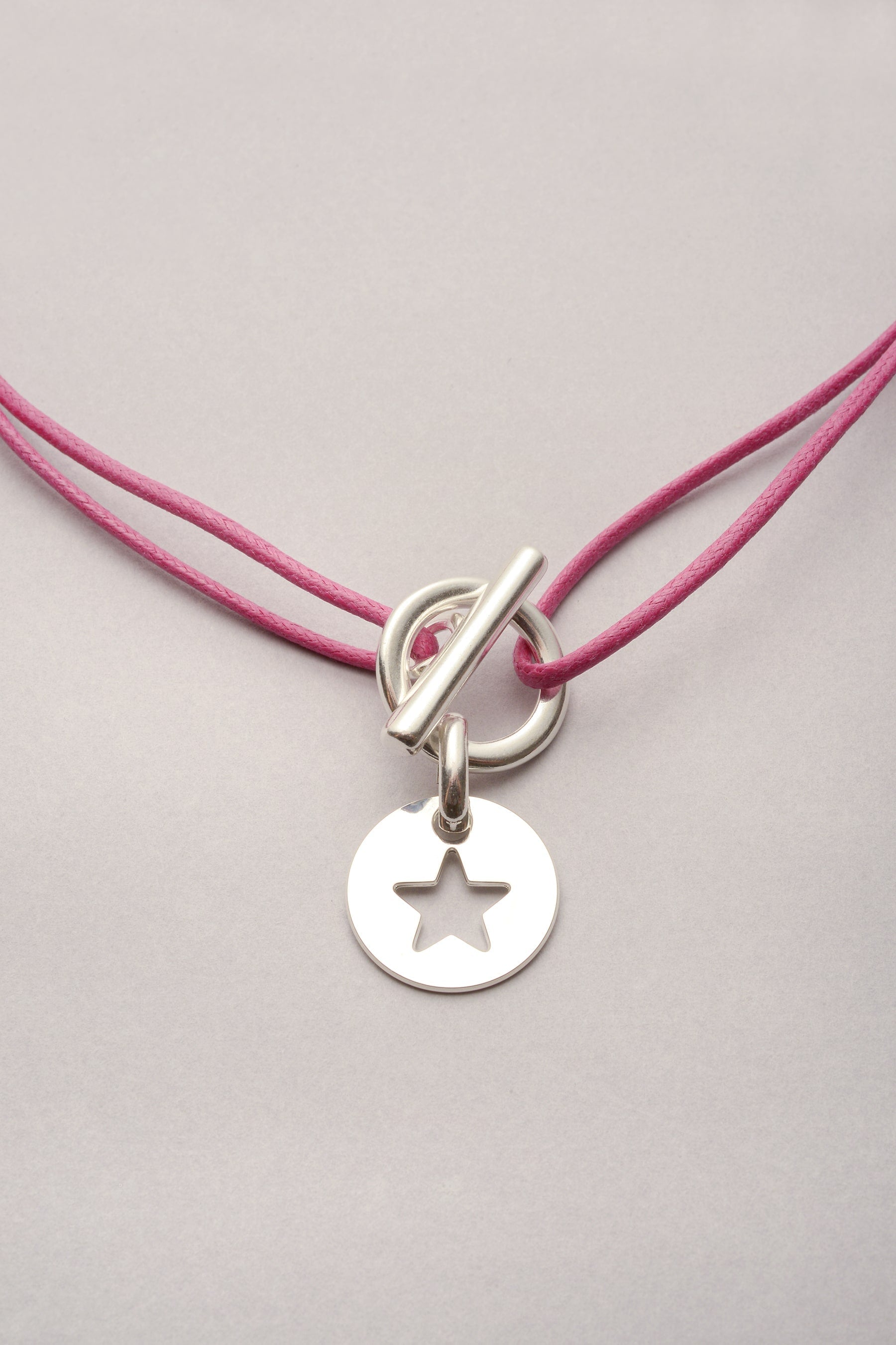 ce collier est composé d'un cordon coloré, d'un fermoir en T et d'un pendentif étoile. L'attache est un fermoir en T qui permet de mettre et enlever le collier de manière pratique. Ce bijou se porte en ras de cou, ou plus long. 