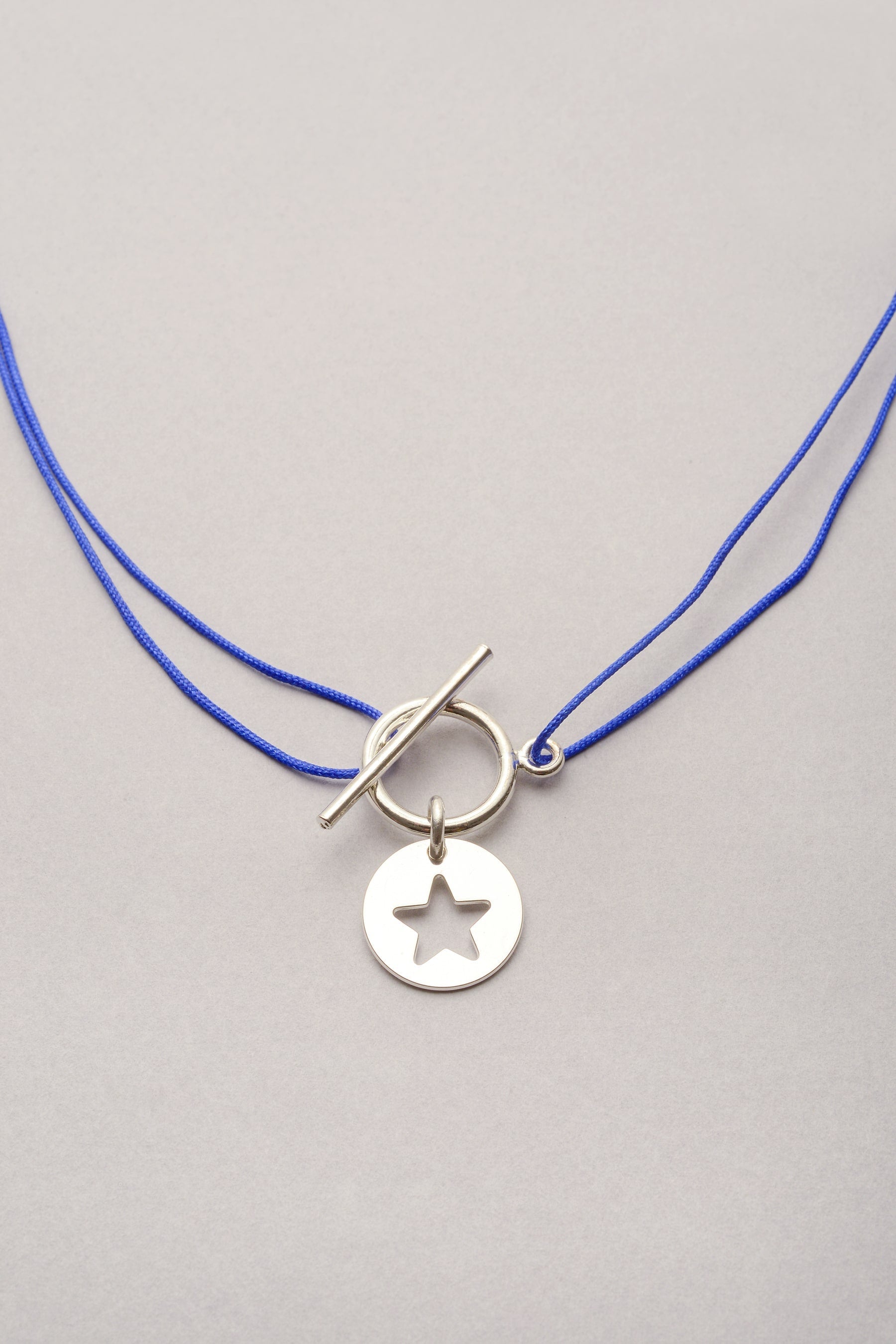 Le collier au cordon fin coloré personnalisable de Musardise. Ce collier réglable  avec sa breloque argentée en forme d'étoile ajourée se porte en ras de cou ou plus long.