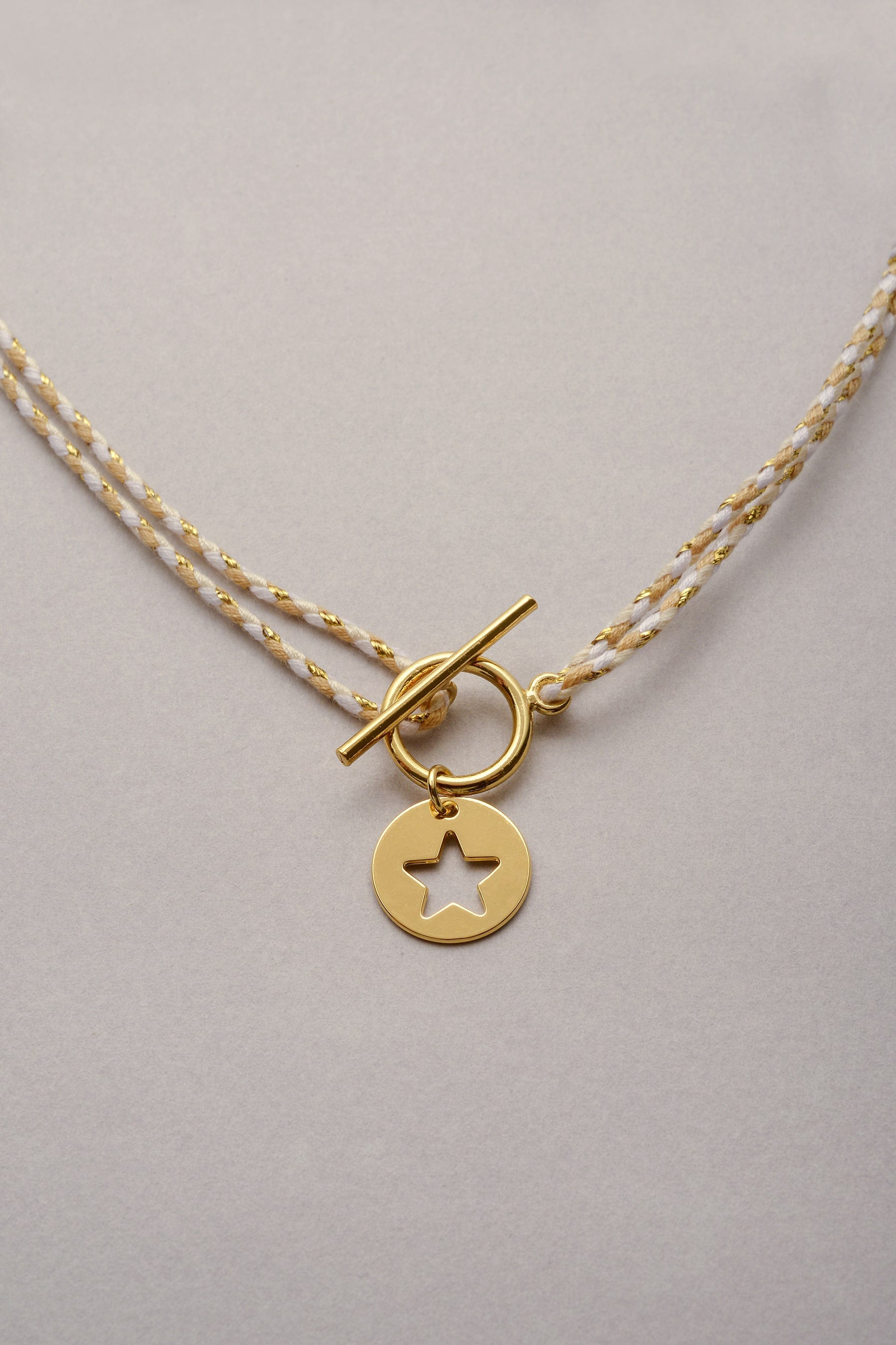 Le collier Lou doré avec sa médaille en forme d'étoile ajouré sur cordon tressé coloré ajustable et son fermoir en T