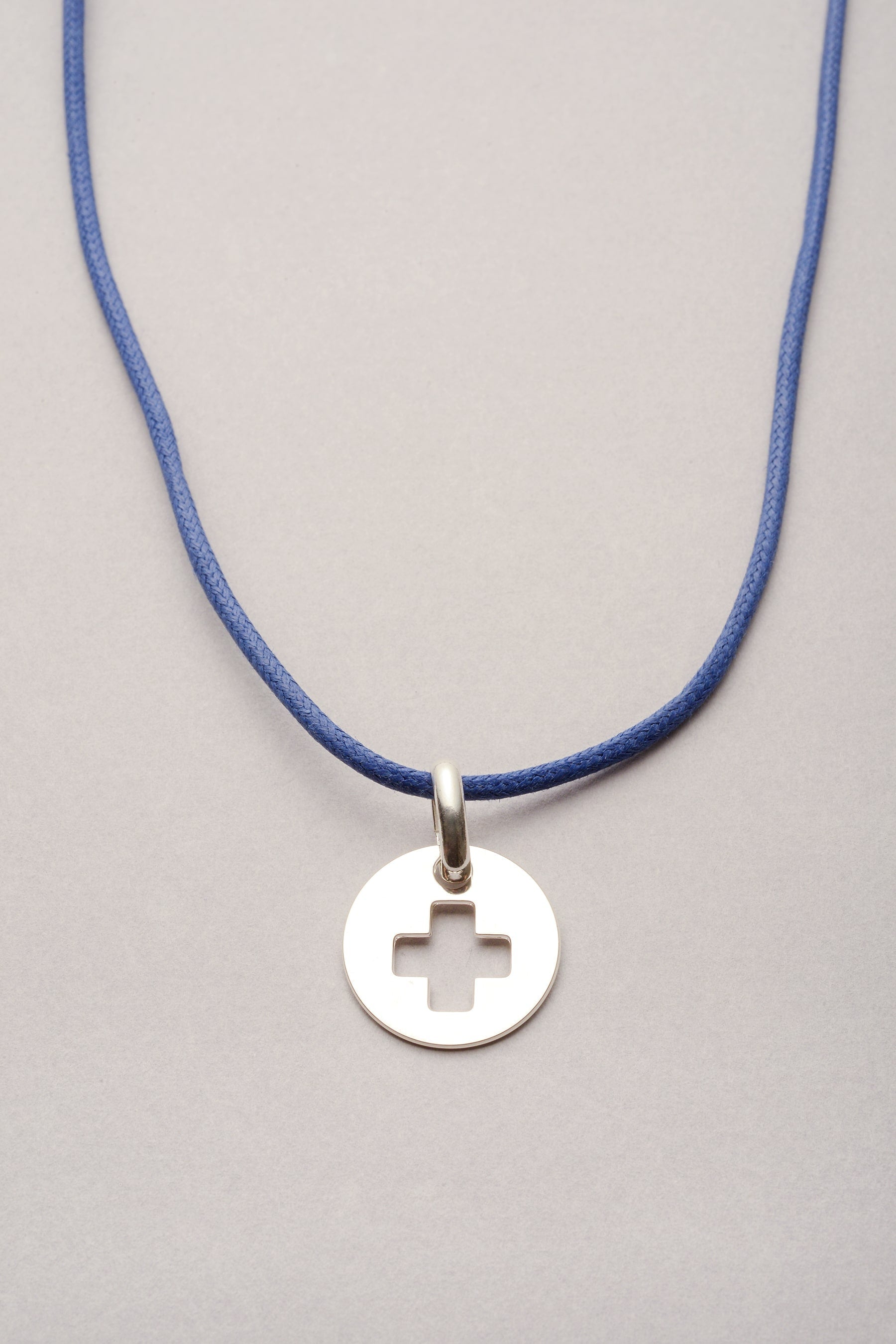 Ce collier est composé d'un cordon coloré réglable et d'une médaille ronde avec une croix évidée. Ce bijou est fabriqué en France et est pas cher. 