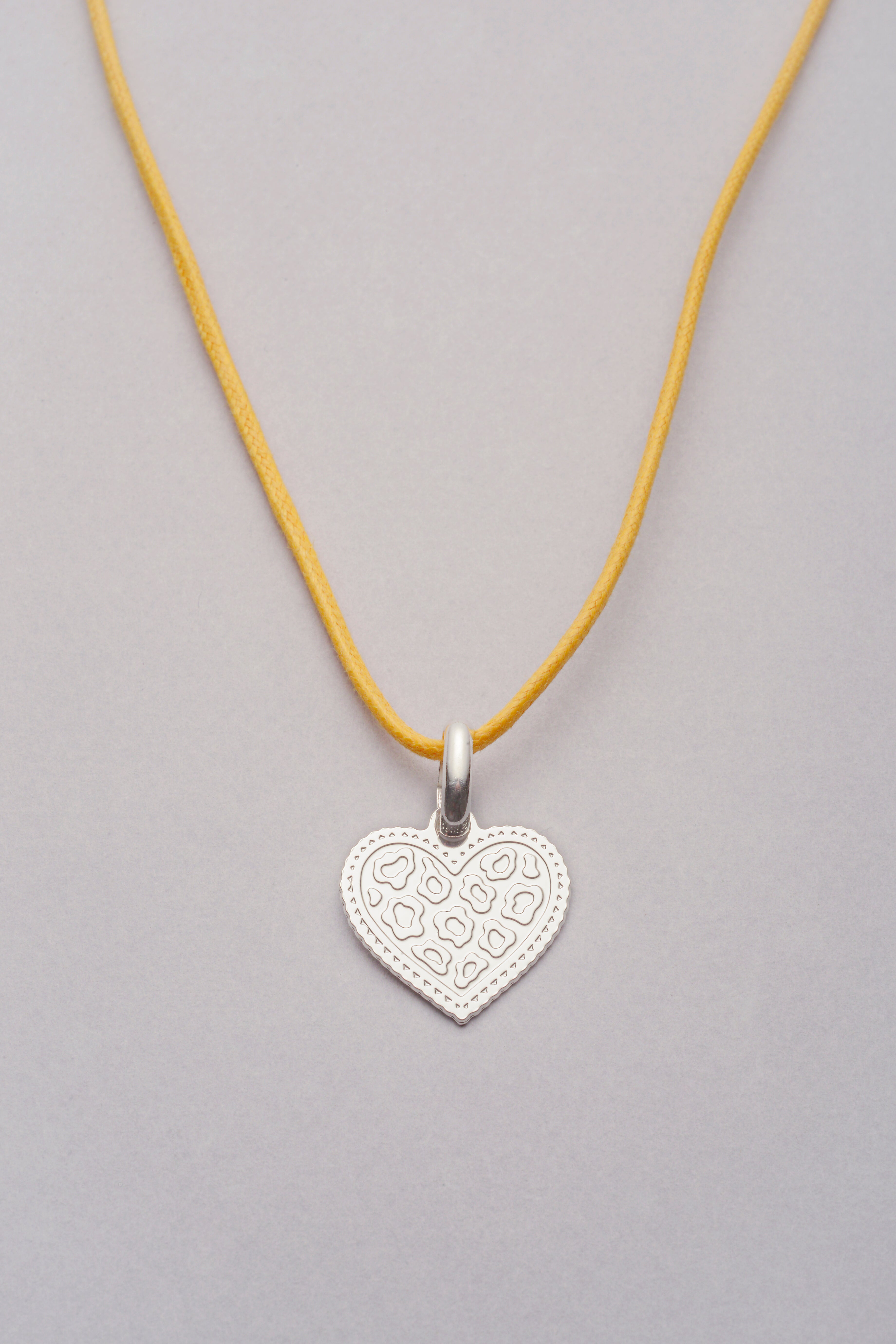 Collier argenté avec pendentif cœur motif léopard, monté sur un cordon coloré réglable, photographié sur fond neutre.