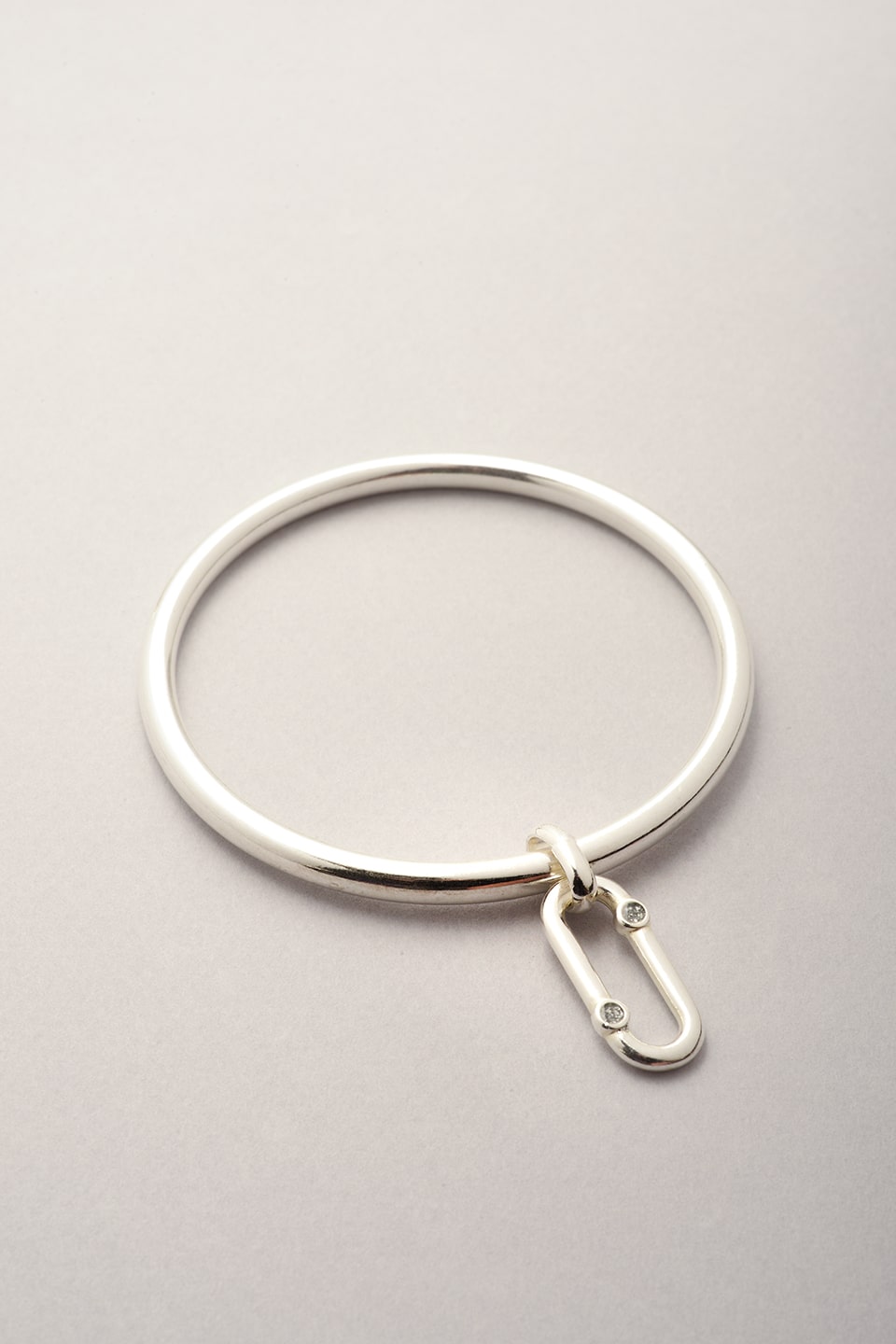 Ce bijou est composé d'un jonc argenté et d'un pendentif oval avec deux strass asymétrique. Bracelet argenté pour femme fabriqué en France. 