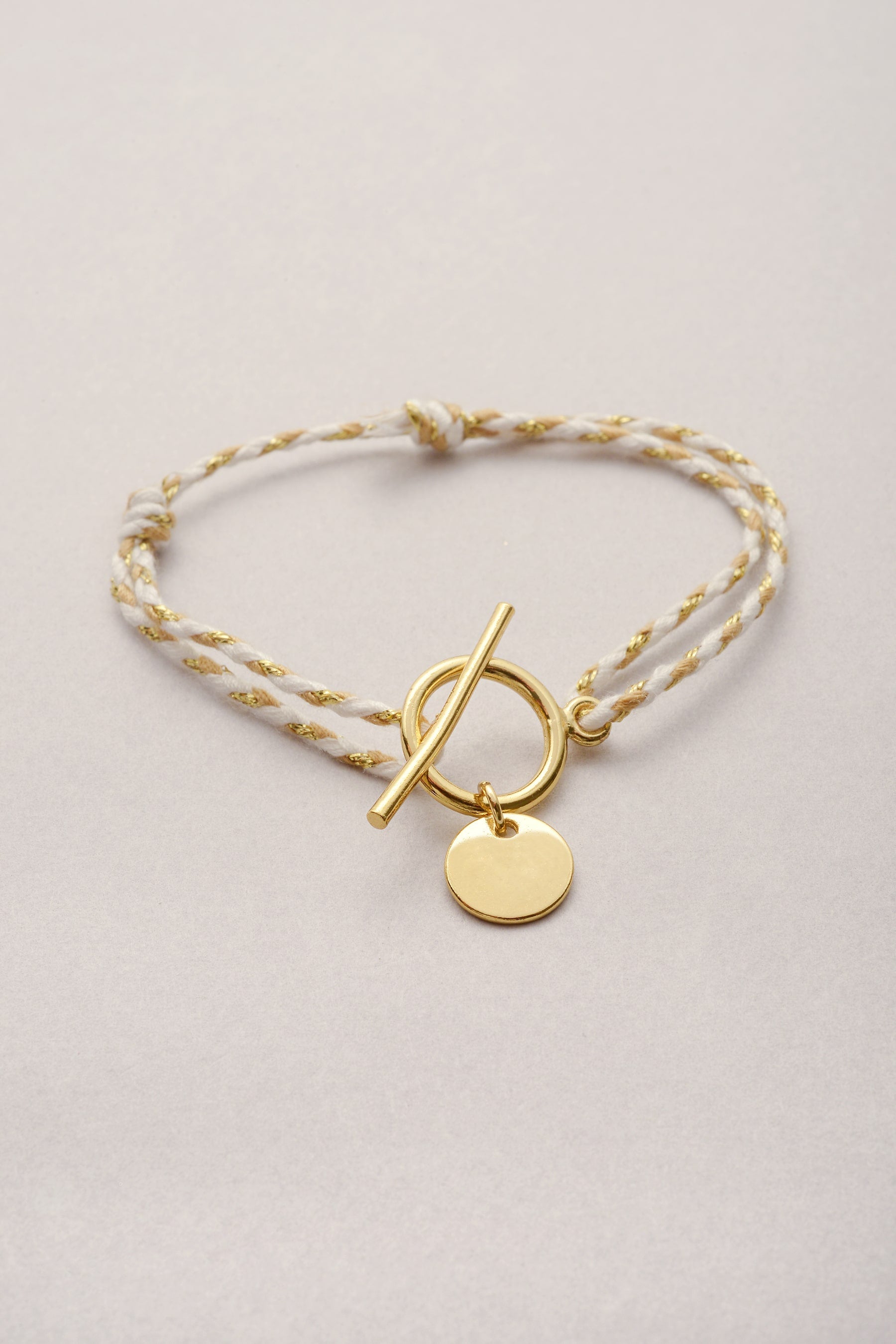 Bracelet en cordon tressé coloré avec sa pampille dorée en forme de coeur ajouré et son fermoir en T.