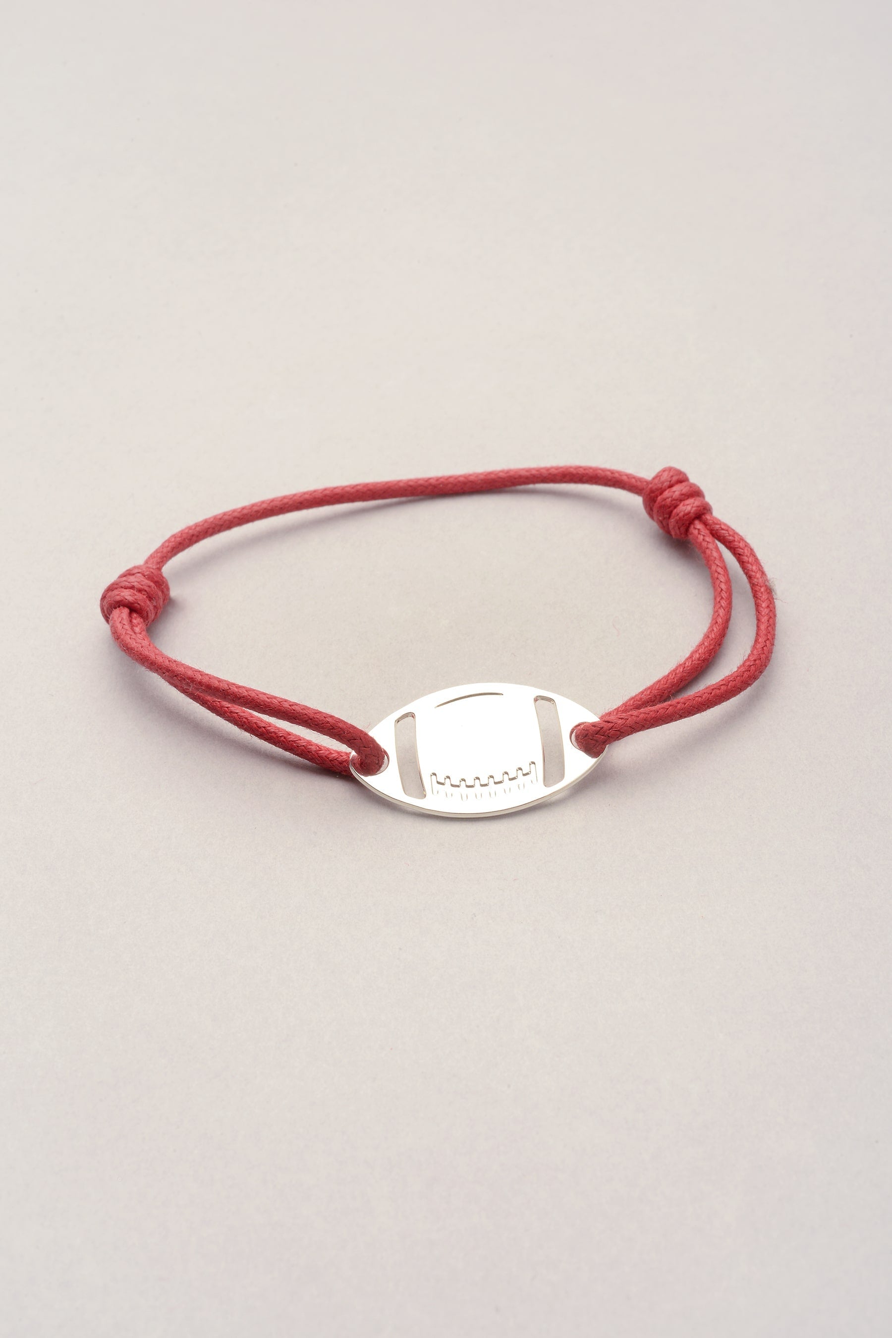 Ce bracelet est composé d'un pendentif en forme de ballon de rugby argenté. Il est ajustable grâce à son cordond e coton coloré réglable. Le pendentif a deux perçage de part et d'autre, le cordon passe dans ceux ci pour faire le tour du poignet. Disponible dans plusieurs coloris et ajustable, vous pouvez l'offrir à un homme ou une femme car il est mixte. 